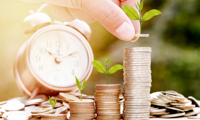 Stack of coins with plants on top of them with an alarm clock in the background