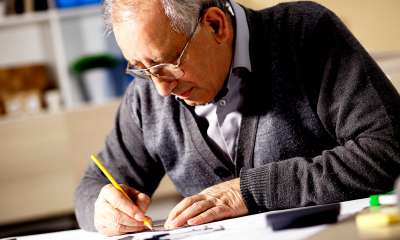 Older man in glasses writing on paper answering his employees questions