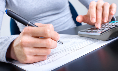 Person in a grey top holding a pen working out their corporation tax using a calculator