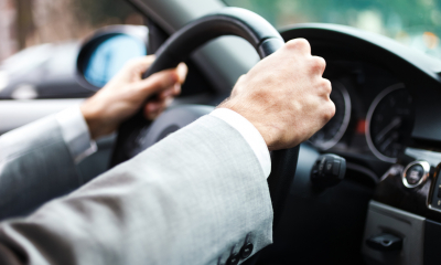 Male employee in a suit with two hands on the steering wheel driving a car