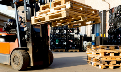 Forklift lifting up multiple wooden pallets with other pieces of machinery in the background