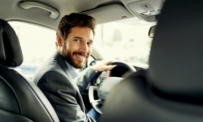 Man in a suit smiling at the camera while driving his company car