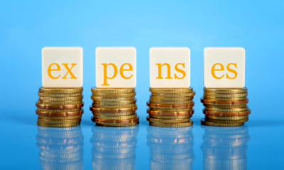 'expenses' written on small tiles balancing on stacks of coins with a blue background
